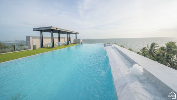 Une piscine à débordement moderne offrant une vue dégagée sur l’océan, un espace salon couvert et une pelouse bien entretenue.