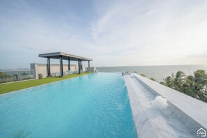 A modern infinity pool with a clear view of the ocean, a covered seating area, and a well-maintained lawn. - Panitar Haus (Chonburi)