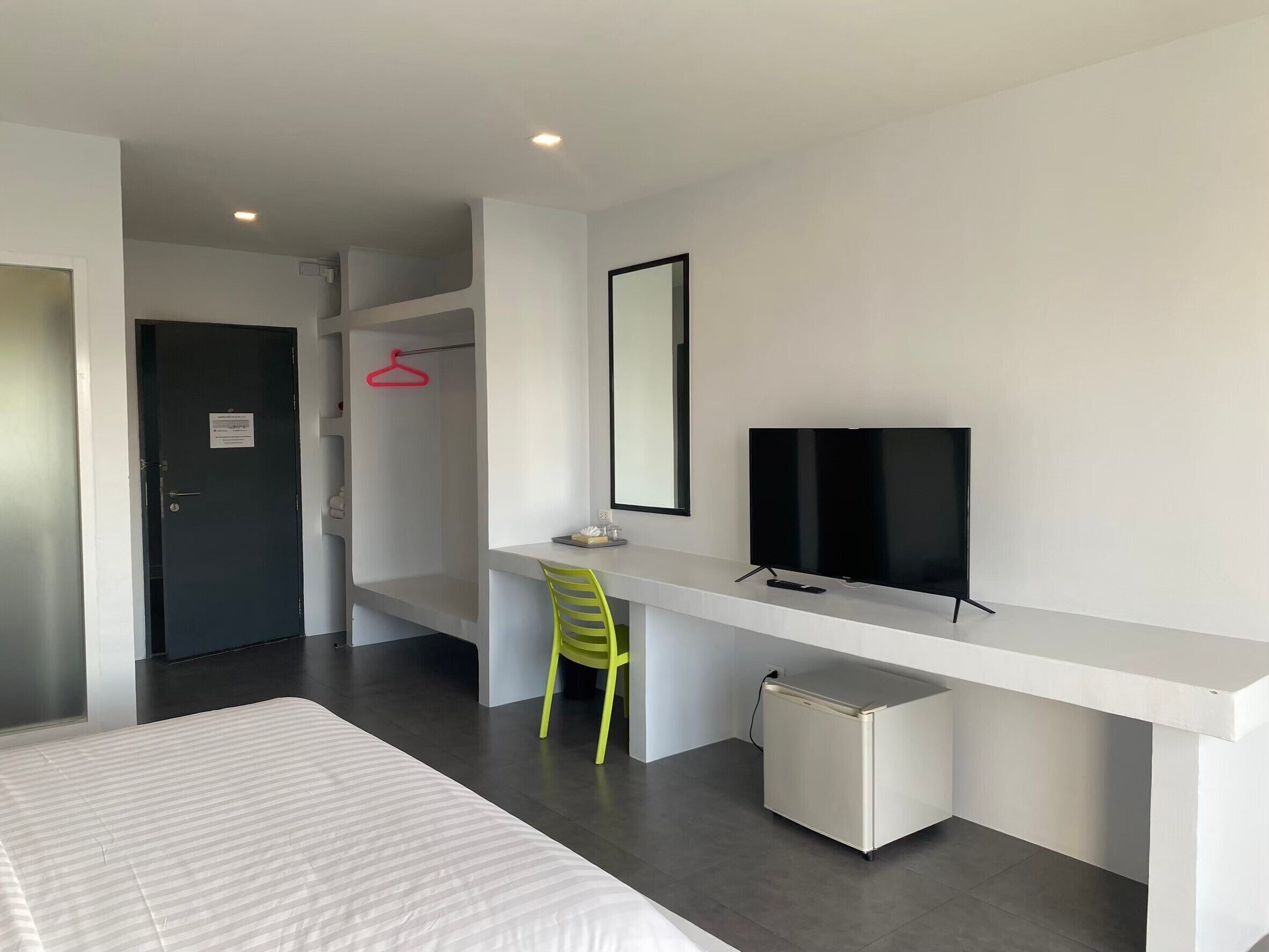 A modern hotel room with a bed, a desk with a chair, a television, and a small refrigerator.
