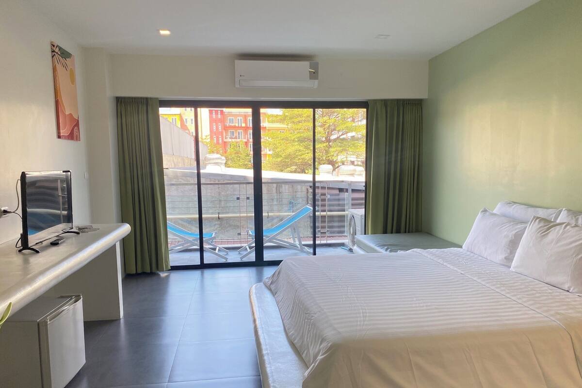 Habitación de hotel con cama, escritorio con computadora y vista a edificios a través de un ventanal.