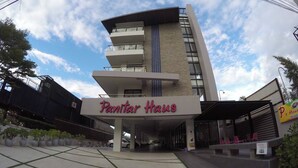 Un bâtiment moderne avec une enseigne indiquant « Panitar Haus » et un espace extérieur abrité avec des chaises rouges.