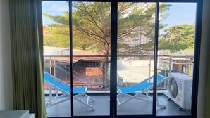 Une pièce dotée d’une grande porte-fenêtre coulissante donnant sur un espace extérieur avec une piscine, des chaises longues et un appareil de climatisation.