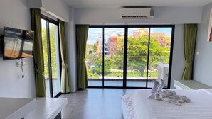 Une chambre d’hôtel dotée d’une grande fenêtre, d’un lit recouvert d’une couette blanche, d’une table de chevet et d’un téléviseur à écran plat fixé au mur.