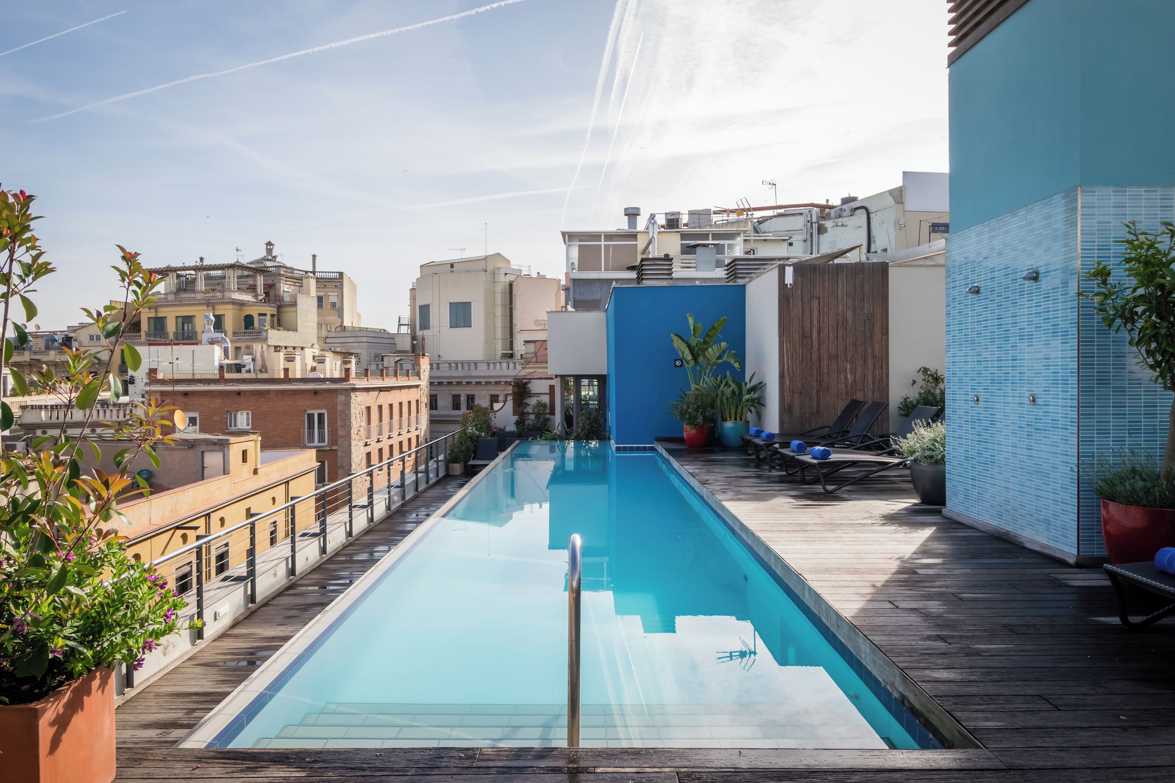 Una piscina en la azotea con un suelo de madera, rodeada de edificios y plantas en macetas.