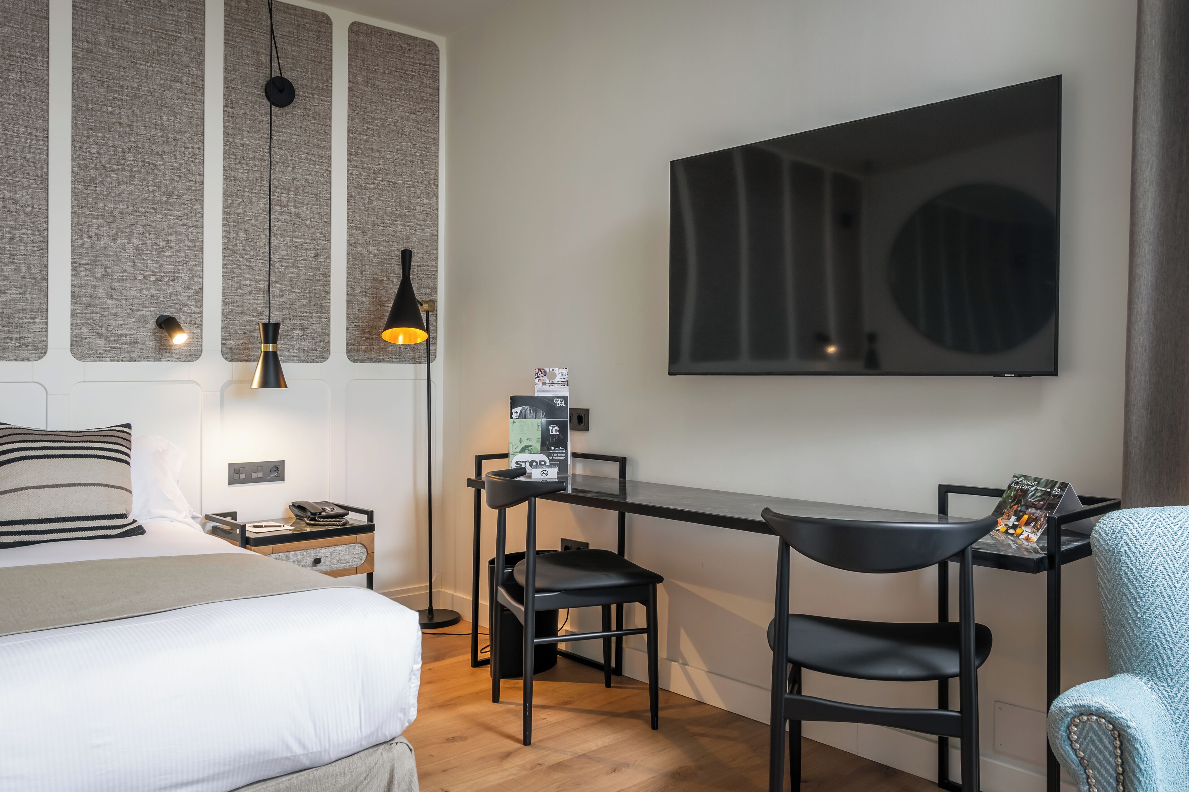 Una habitación de hotel moderna con cama, escritorio, dos sillas, televisión y un amplio ventanal.