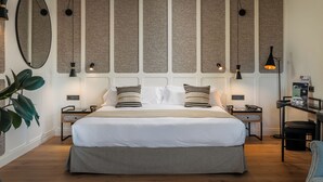 A modern hotel room with a large bed, two bedside tables, a desk with a chair, a large mirror, and a wall with vertical panels. - Hotel Barcelona Catedral (Barcelona)