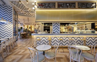 A restaurant interior with a bar area, wooden flooring, and white chairs.