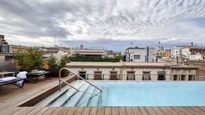 A rooftop pool with wooden deck and lounge chairs, surrounded by urban buildings and a cloudy sky. - Hotel Barcelona Catedral (Barcelona)