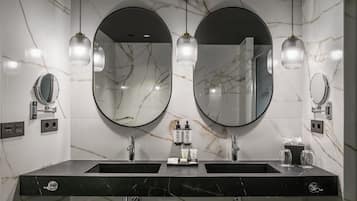 A bathroom with two sinks, marble walls, and two round mirrors.