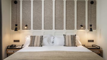 A neatly made bed with white linens and striped pillows, a bedside table with a phone, and a wall with vertical panels and hanging lights.
