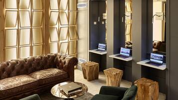 Una sala de estar moderna con un sofá de cuero, sillones verdes y una mesa de centro. Hay taburetes de madera y una computadora portátil sobre una plataforma de madera.