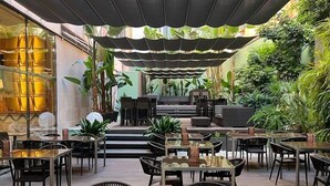 An outdoor dining area with tables and chairs, surrounded by greenery and a covered seating area. - Hotel Barcelona Catedral (Barcelona)