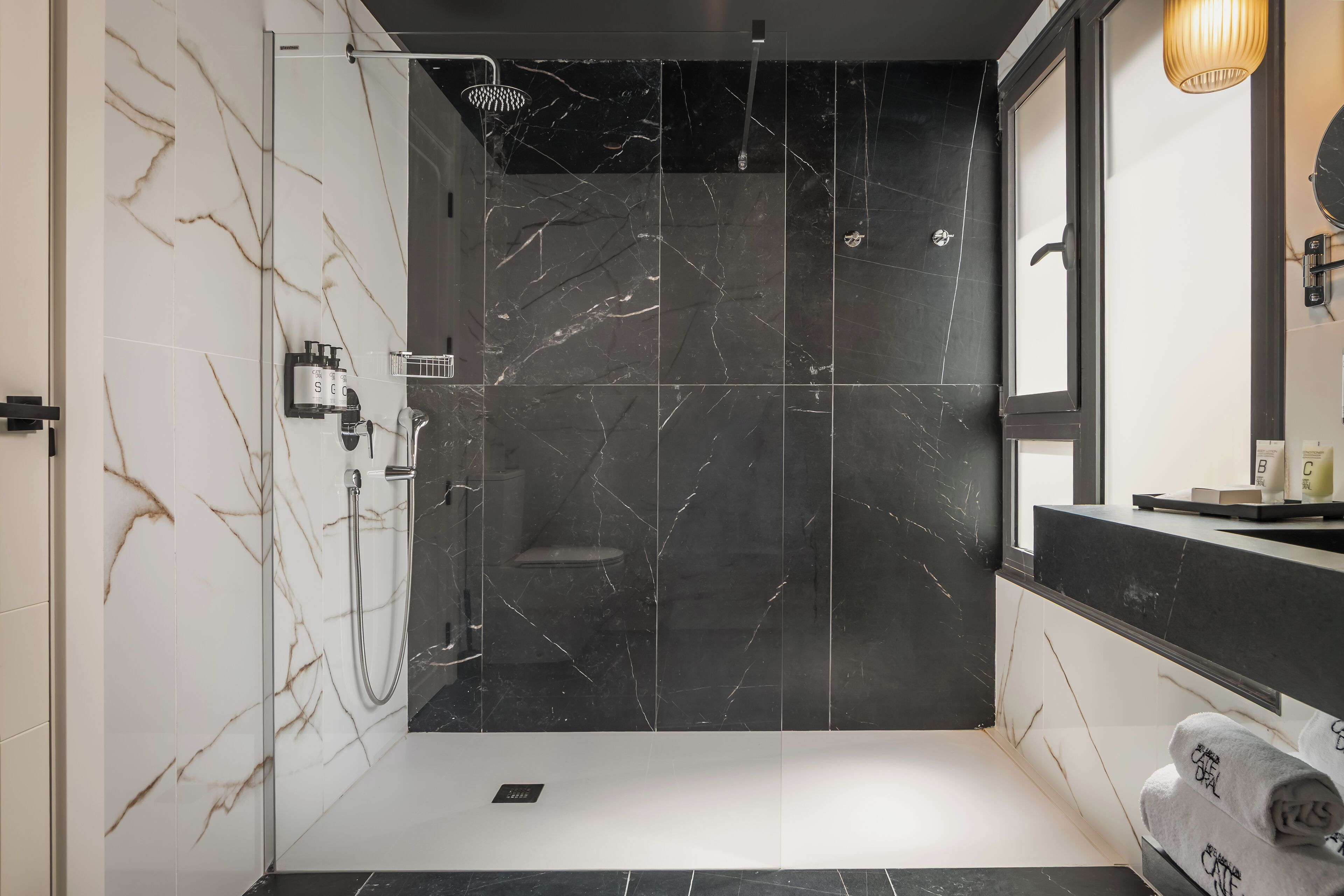 A modern bathroom with a glass-enclosed shower, marble walls, and a black countertop with a mirror.