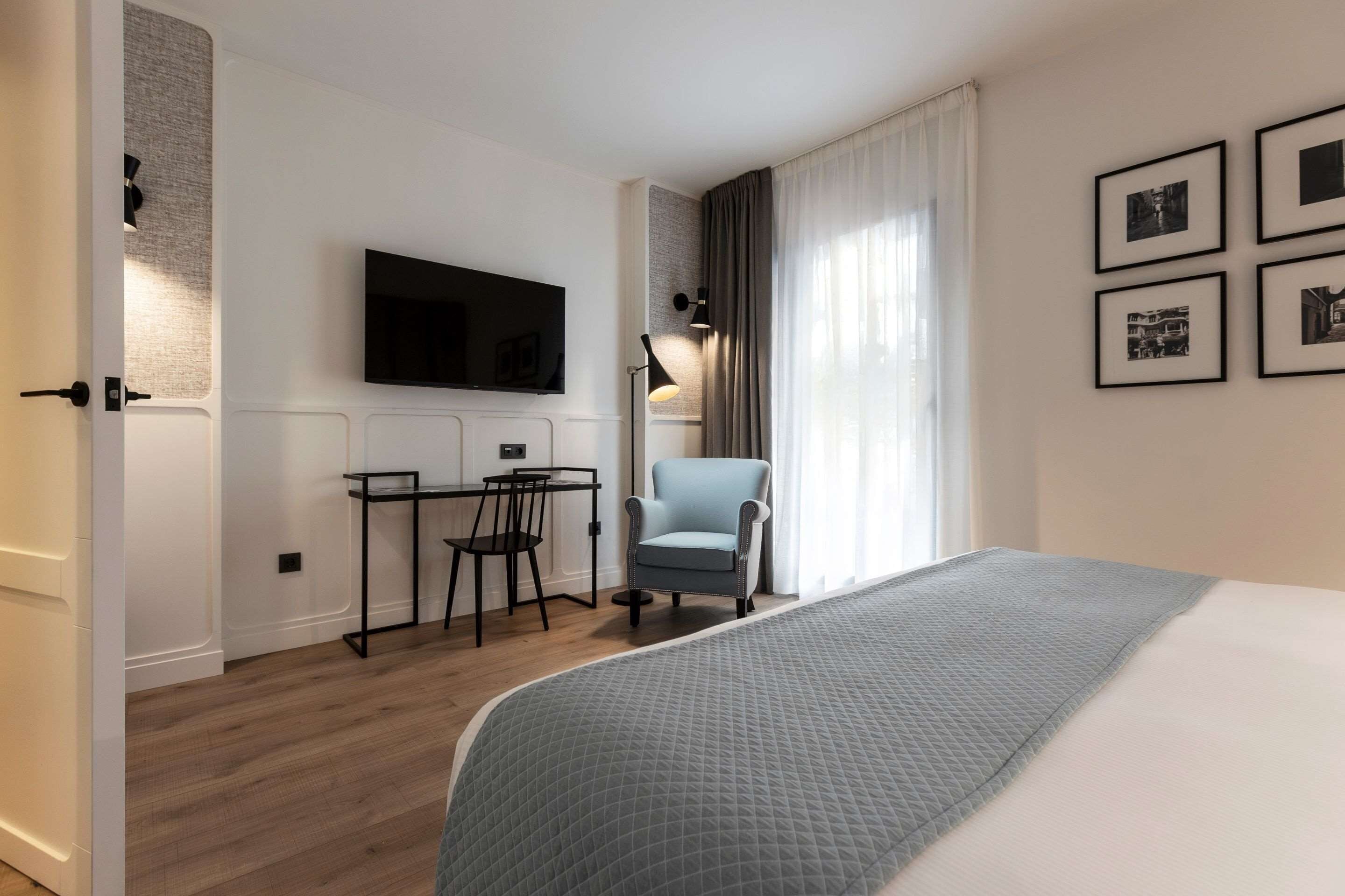 A modern hotel room with a large bed, a desk with a chair, a television, and framed pictures on the wall.