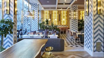 A modern restaurant with a long wooden bar, gold bar stools, and a herringbone patterned floor.