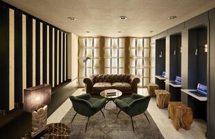 A modern lounge area with a leather sofa, two green armchairs, a marble coffee table, and a wooden side table.