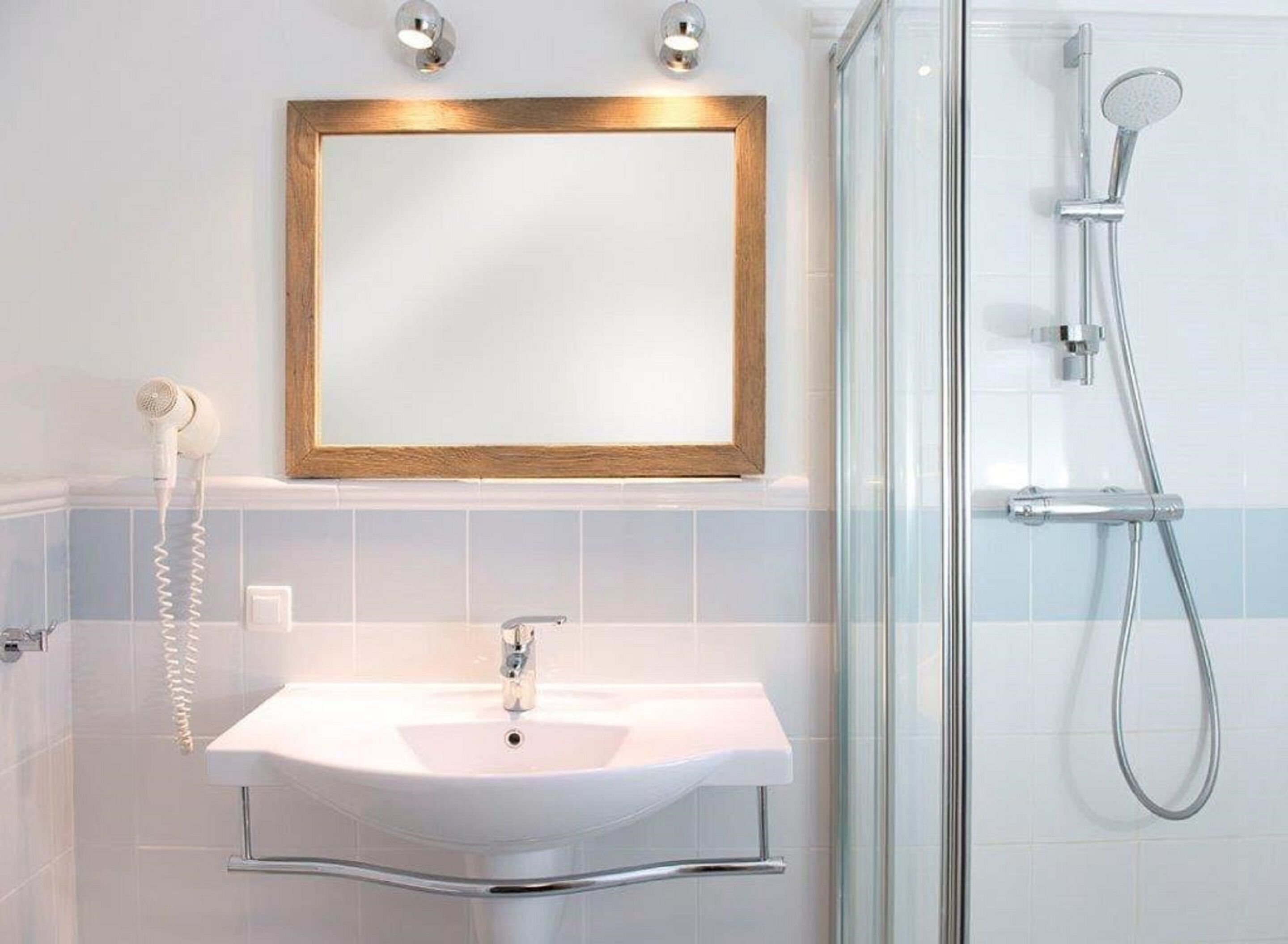 Ein Badezimmer mit einem weißen Waschbecken, einem gerahmten Spiegel, einer Handbrause und einer Duschkabine aus Glas.