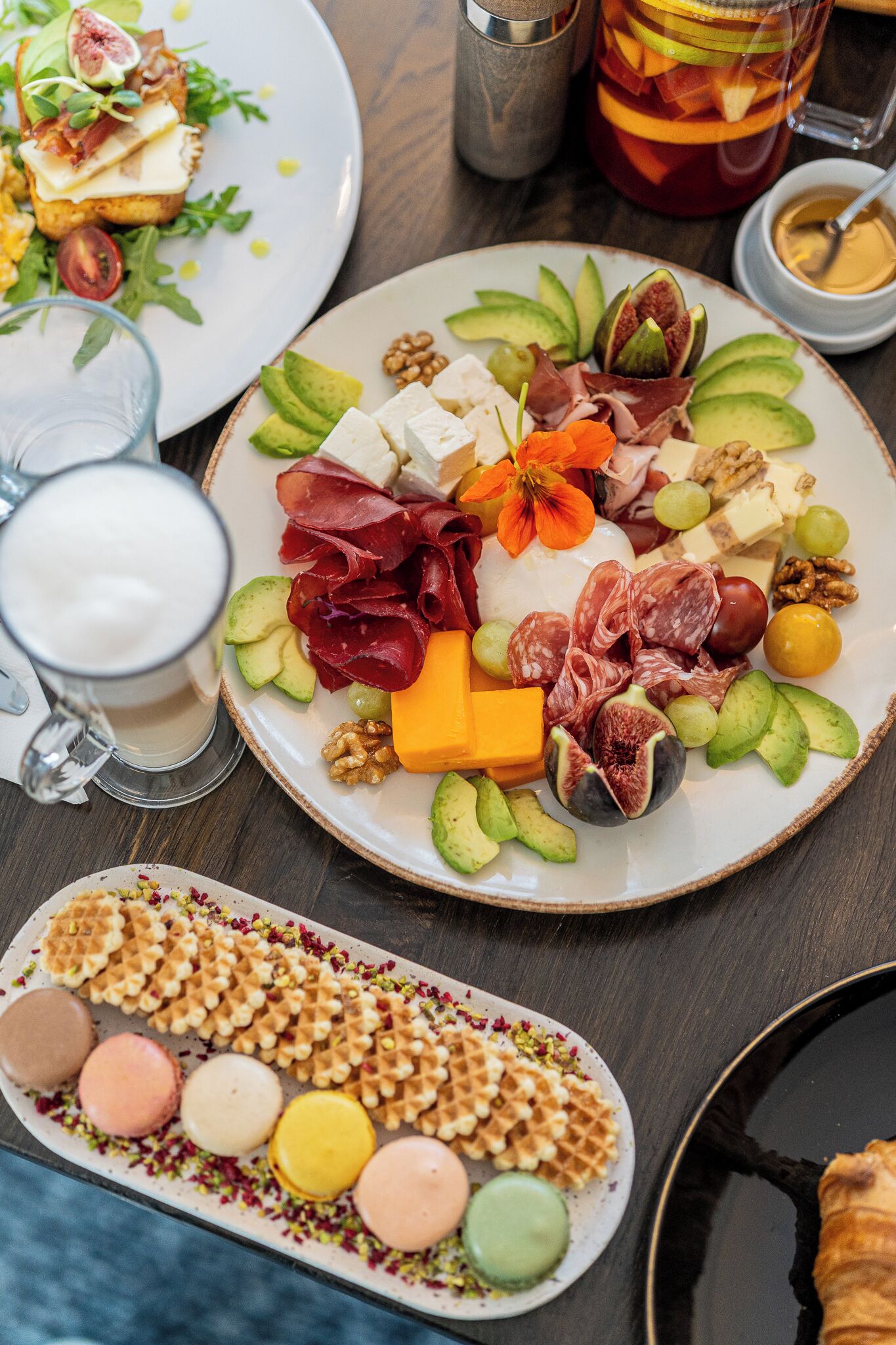 A plate of assorted cheeses, meats, and fruits, a glass of milk, and a tray of macarons.
