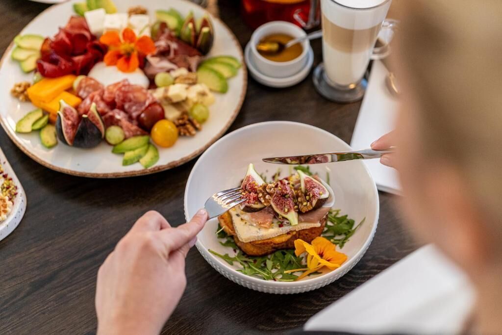 Uma mesa de jantar com um prato de queijos, frutas e carnes variadas, e uma tigela com um sanduíche.