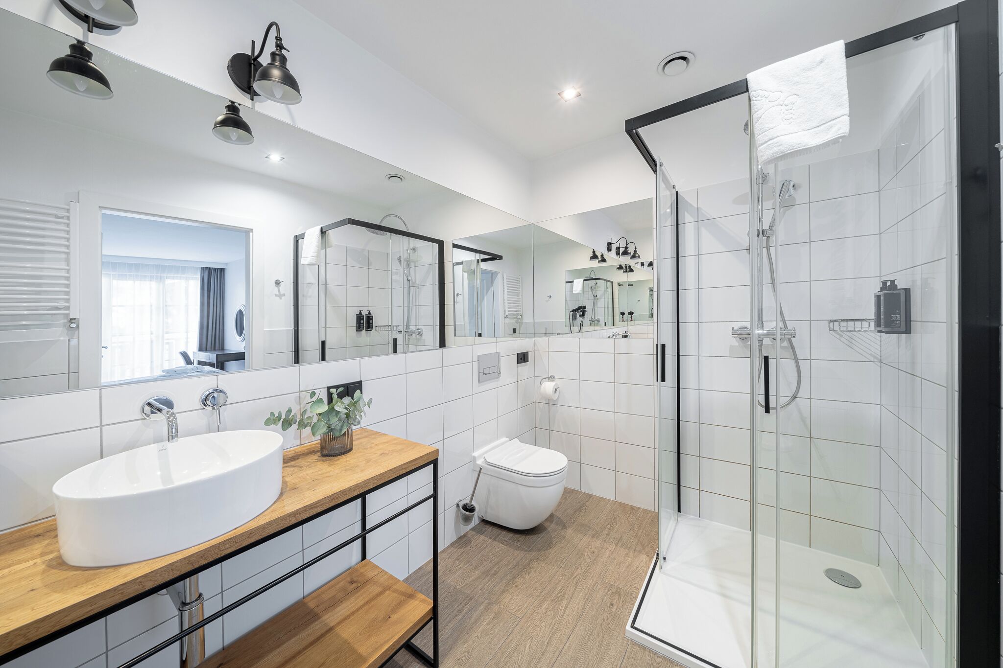 A modern bathroom with a large mirror, a sink, a toilet, and a glass-enclosed shower.