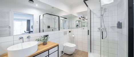 A modern bathroom with a large mirror, a sink, a toilet, and a glass-enclosed shower.