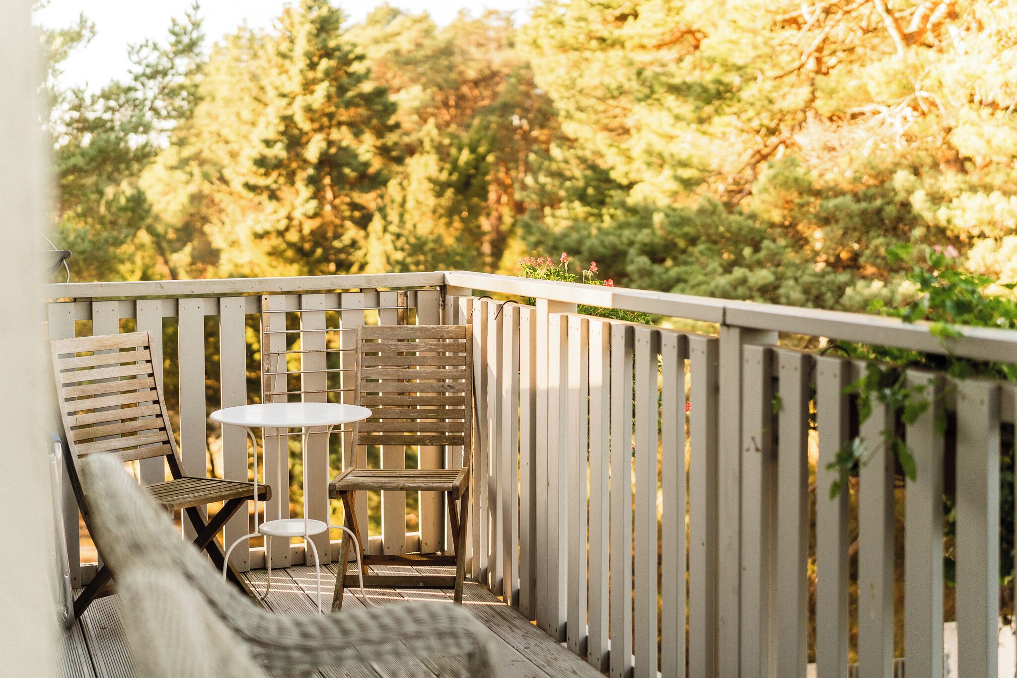 A wooden deck with a white table and two chairs, surrounded by a white fence.