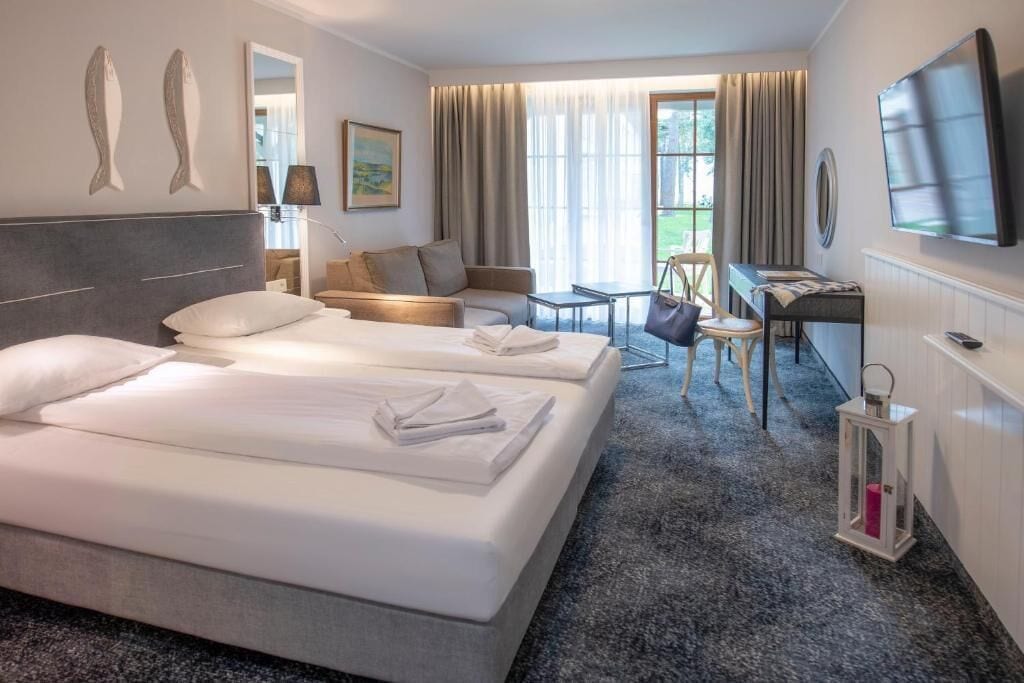 Une chambre d’hôtel avec deux lits, un bureau, une chaise, une télévision et une fenêtre avec des rideaux.