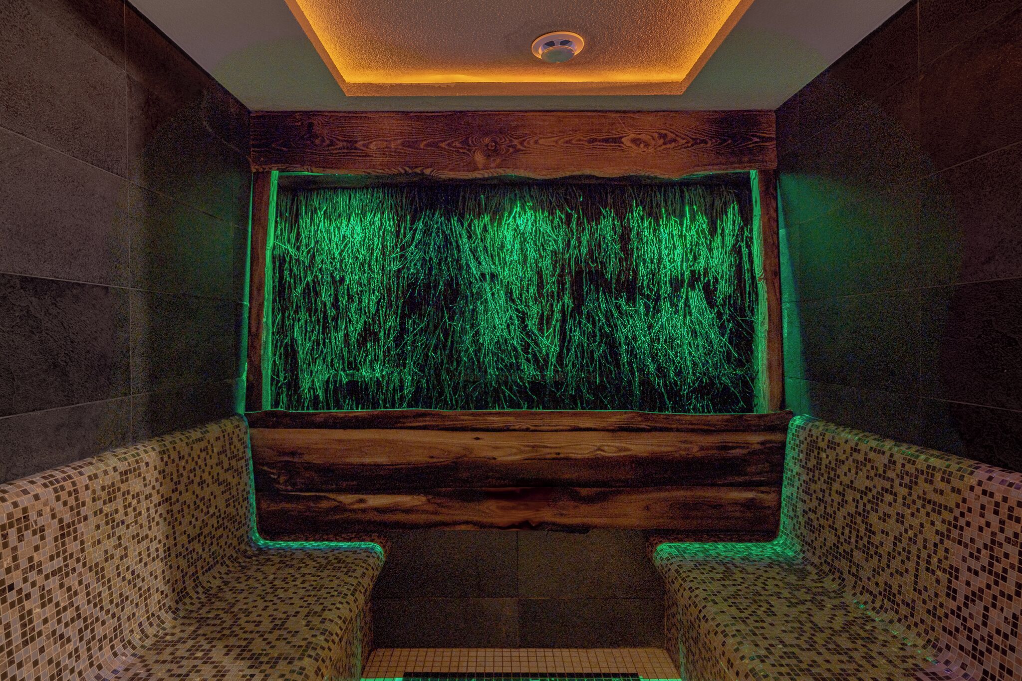 A spa room with a wooden bench, a wall with a green light feature, and a ceiling with a recessed light.