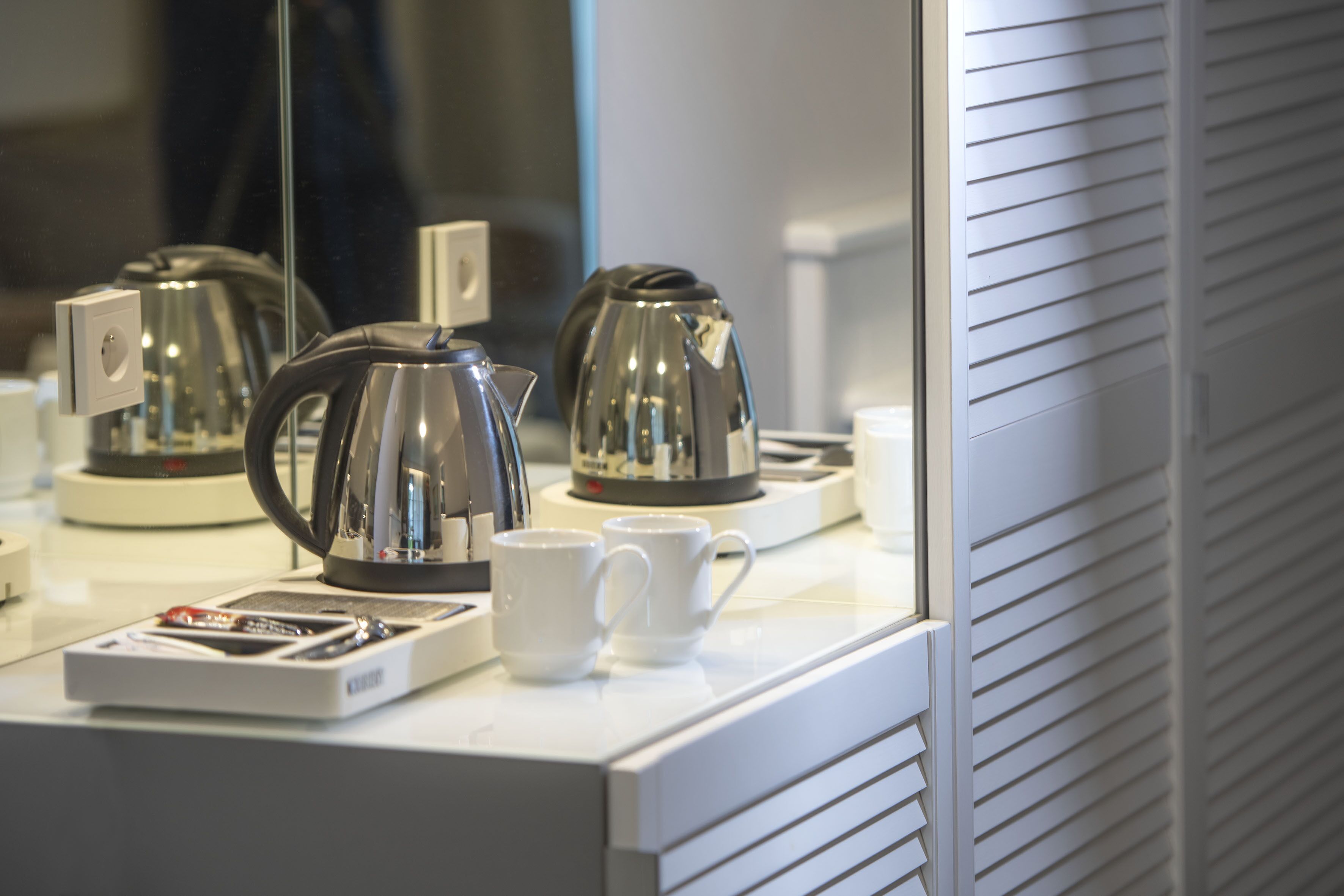 A coffee station with a kettle, cups, and a coffee maker on a countertop.