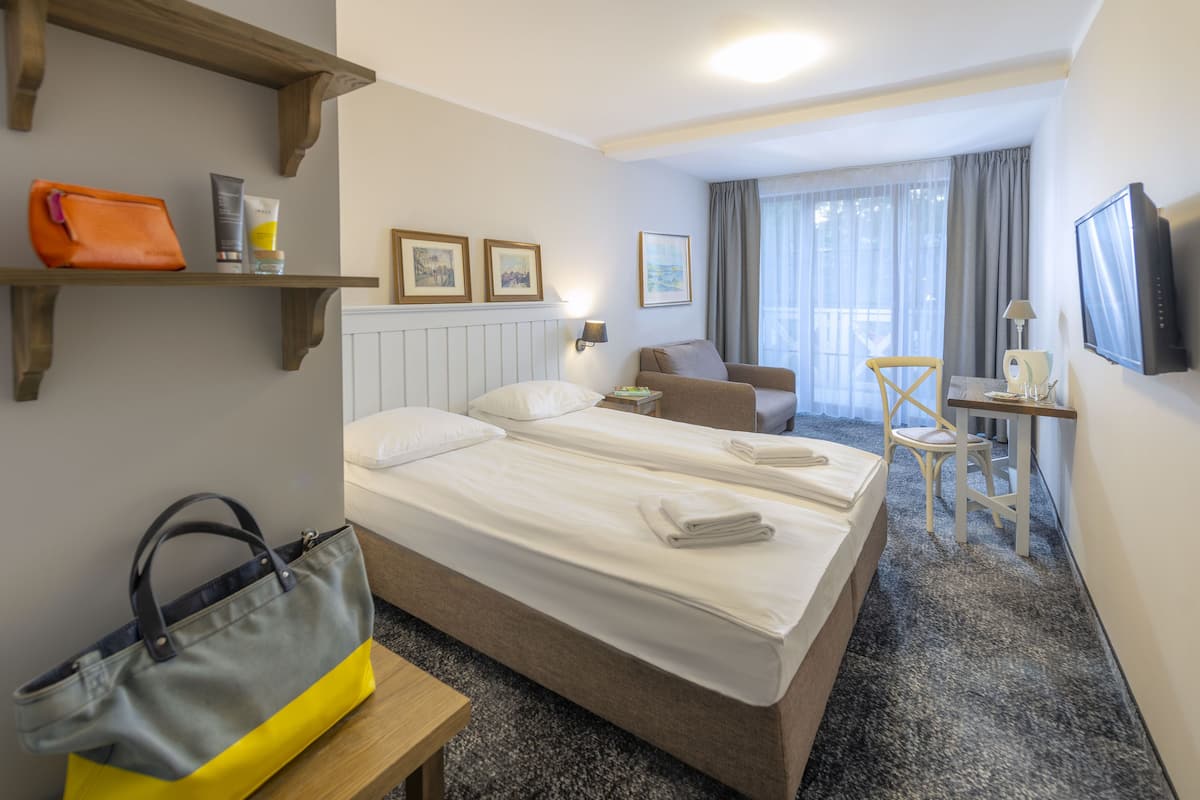 A hotel room with a bed, a desk, a chair, a TV, and a window with curtains.