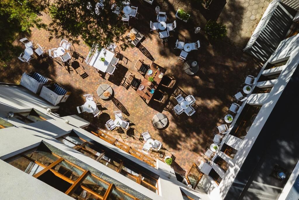 Vista aérea de un patio con mobiliario exterior, mesas y sillas dispuestas alrededor de una zona central con un brasero.