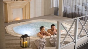 Una pareja relajándose en un jacuzzi con velas y un estante de madera con adornos.