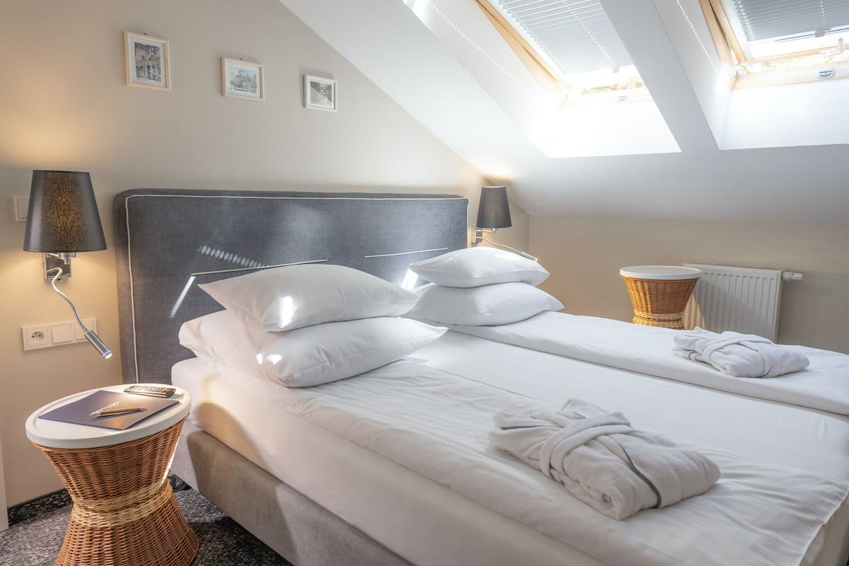A hotel room with a large bed, two bedside tables, a lamp, and a view of the sky through skylights.