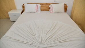 Una cama bien tendida con dos almohadas, un cabecero de madera y una mesita de noche blanca con cajones.