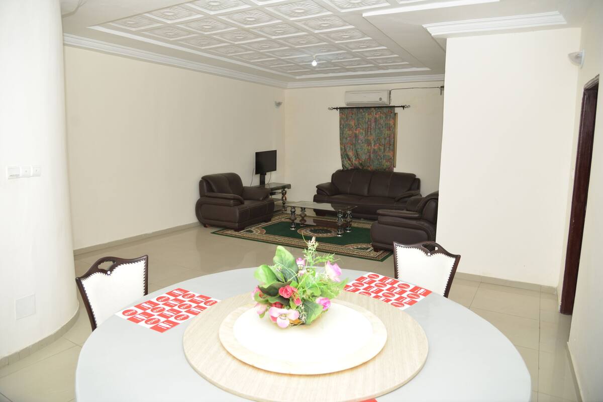 A dining area with a round table, chairs, a floral centerpiece, and a television in the background.