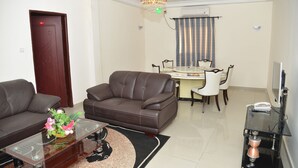 Una sala de estar con un sofá marrón, una mesa de centro de vidrio con un centro de mesa floral y un comedor con mesa y sillas.