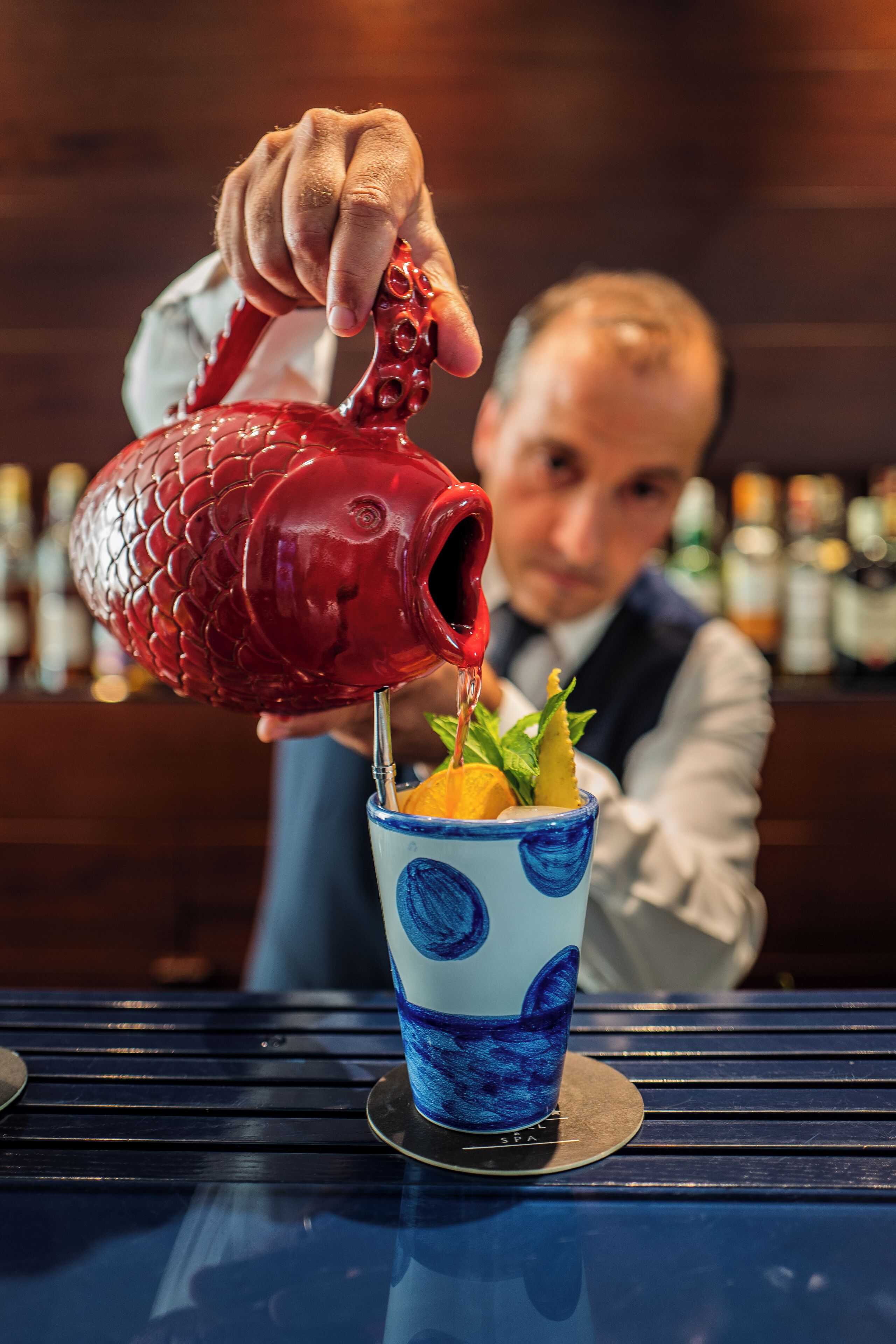 A bartender pouring a drink into a blue and white cup with a fish design.
