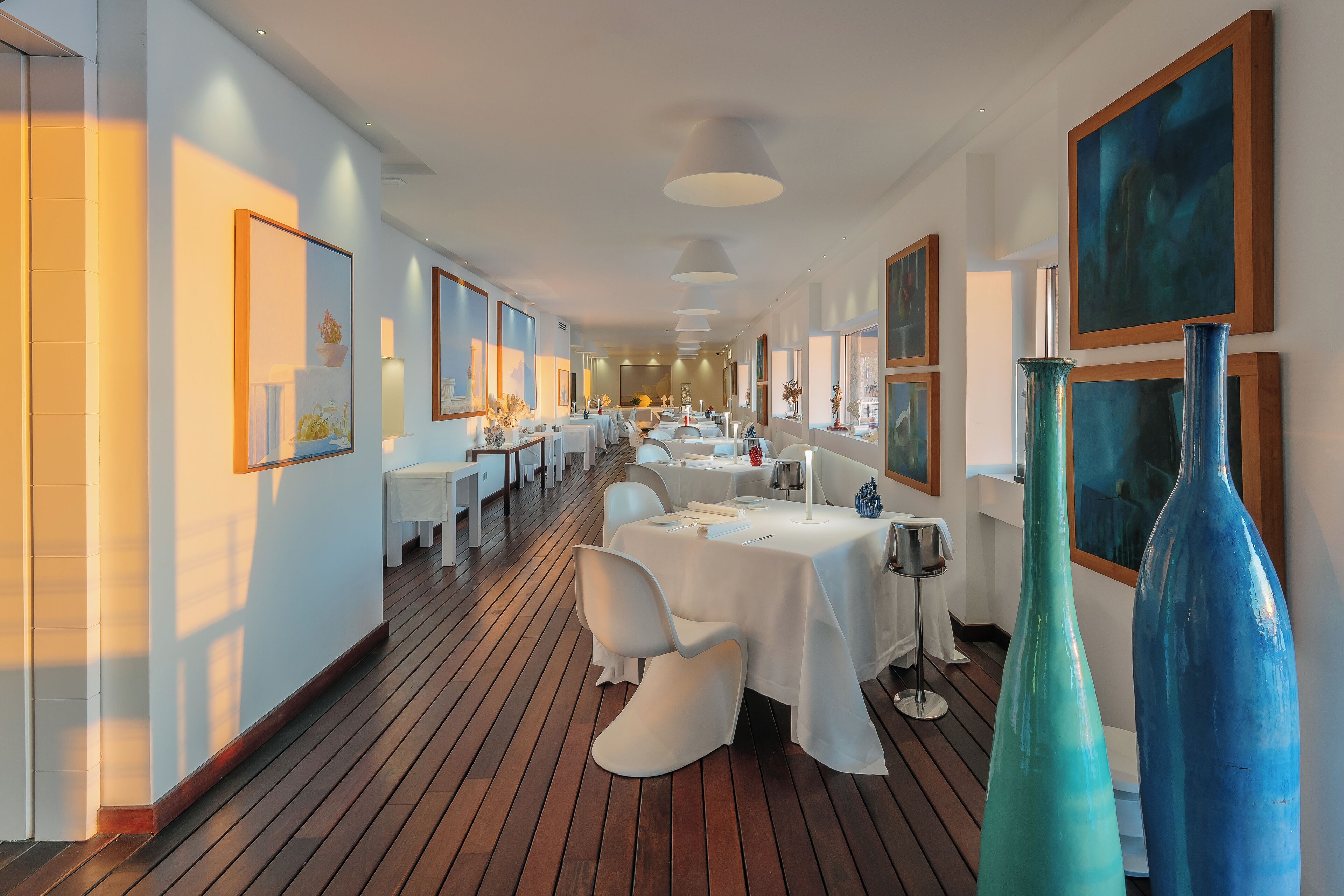Ein modernes Restaurant mit weißen Tischen und Stühlen, Holzböden und großen Bildern an den Wänden.