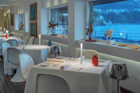 A restaurant with white tables and chairs, lit by modern lamps, and decorated with flowers and candles. - Capo La Gala Hotel & Wellness (Vico Equense)