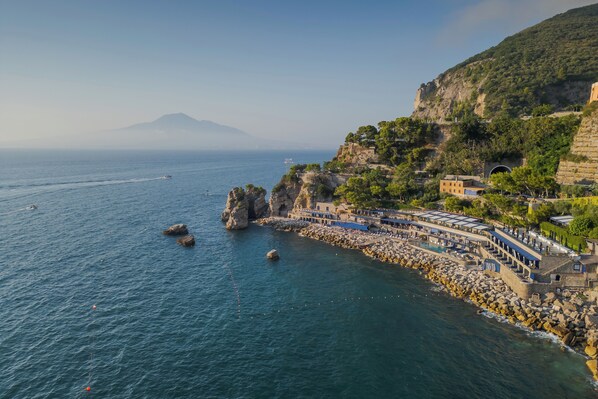 A coastal hotel with a rocky shoreline, a pool, and a mountain in the background. - Capo La Gala Hotel & Wellness (Vico Equense)