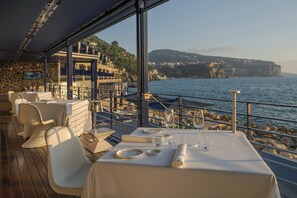 A dining area with tables set for two, overlooking a coastal landscape with rocky cliffs and a body of water. - Capo La Gala Hotel & Wellness (Vico Equense)