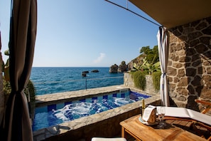 A stone-walled infinity pool with a clear view of the sea, a wooden table with a bottle and glass, and a chair. - Capo La Gala Hotel & Wellness (Vico Equense)