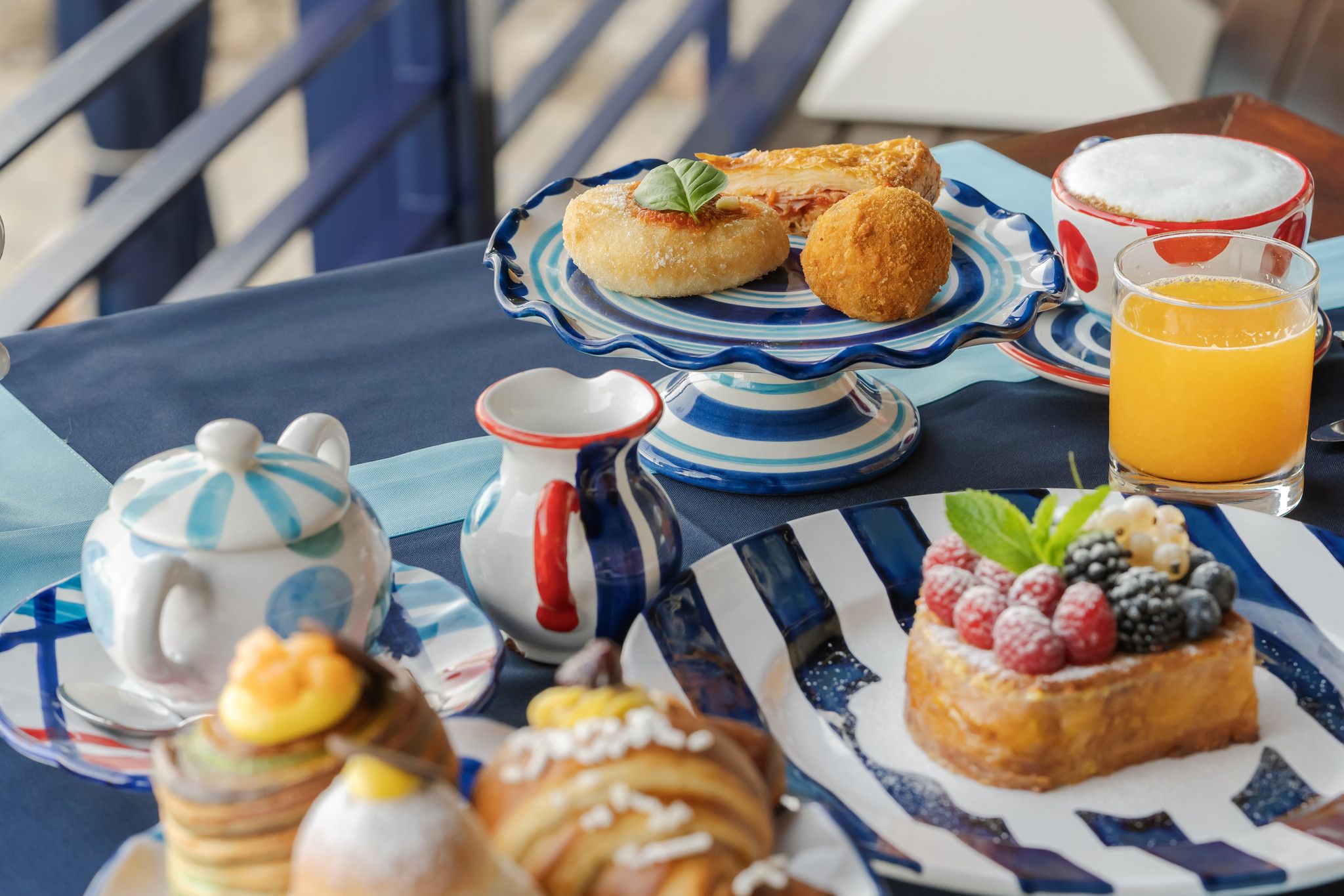 A table set with breakfast items including pastries, a fruit-topped dessert, a glass of orange juice, and a teapot.