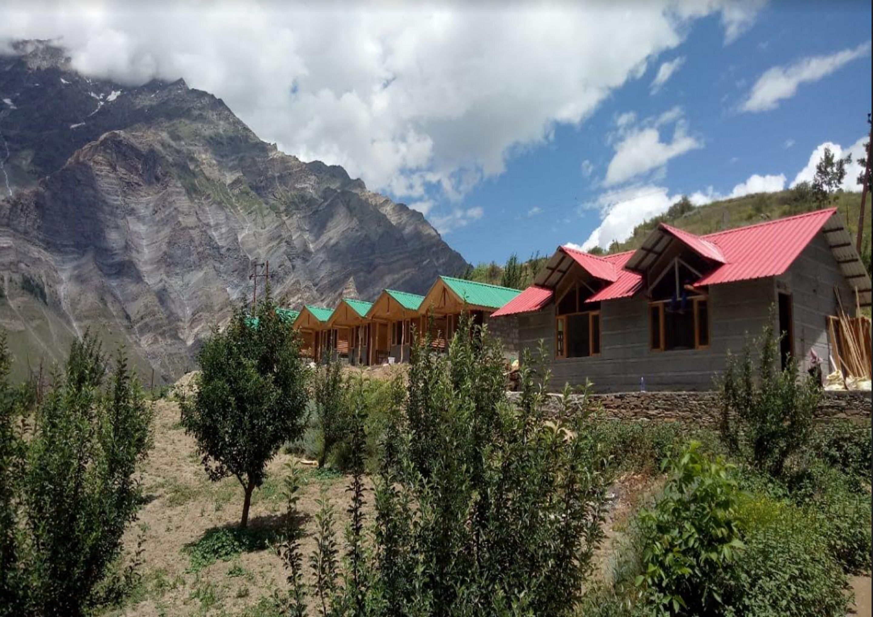 A row of wooden cabins with red roofs, set against a mountainous backdrop.