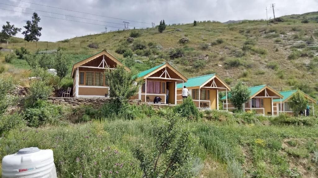 A row of wooden cabins with green roofs, set on a grassy hillside.