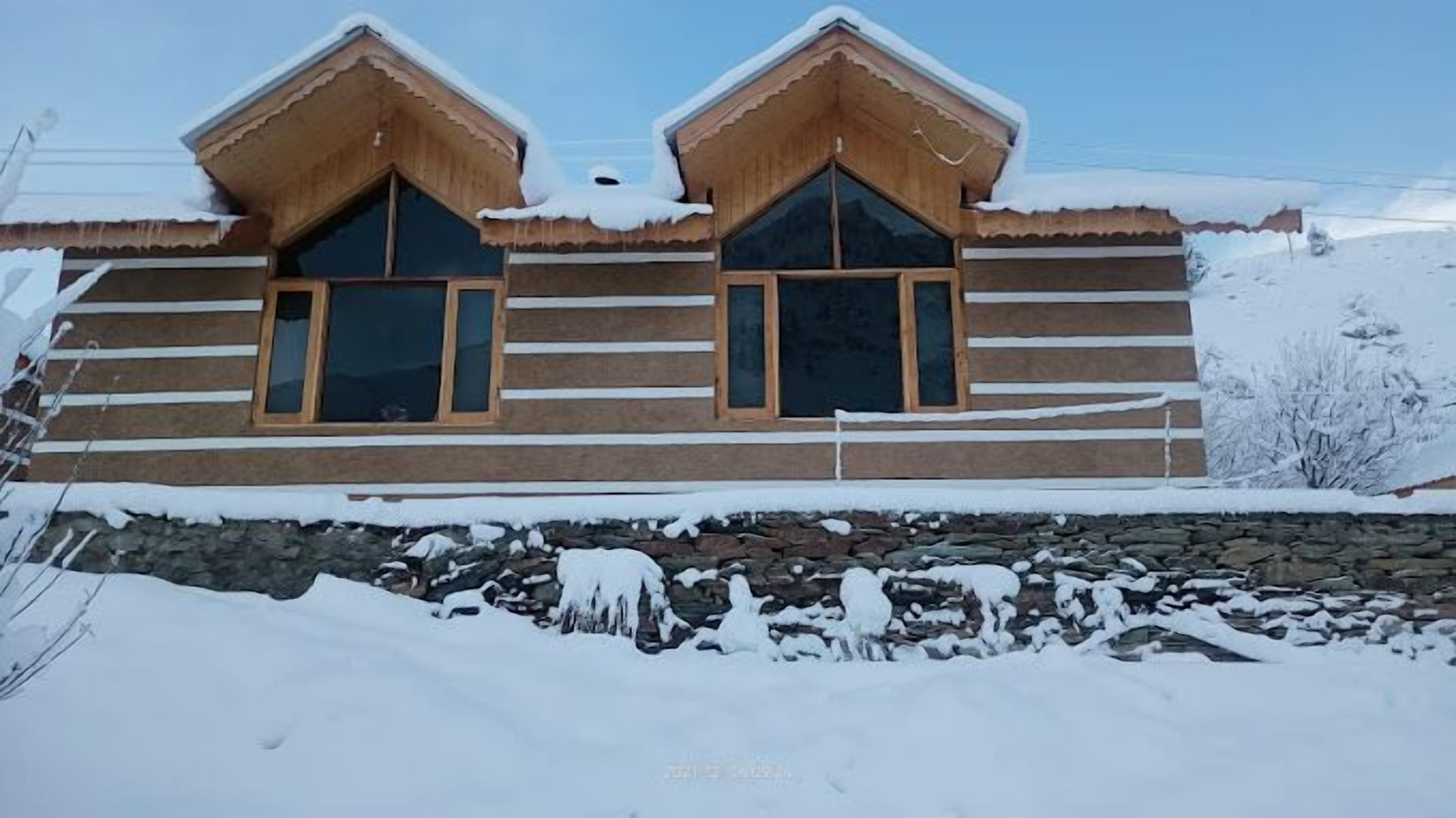 A log cabin with two large windows and a stone foundation.