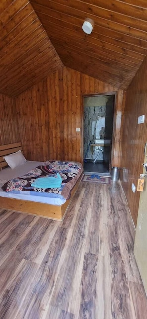 A wooden cabin bedroom with a bed, wooden flooring, and a door leading to a bathroom. - Tandi Sarai (Spiti)