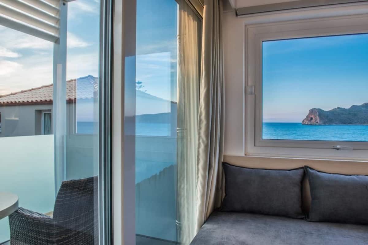 A balcony with a glass door, a sofa with cushions, and a view of the sea and mountains.