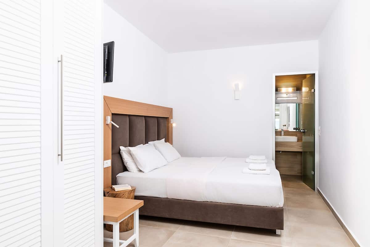 A modern bedroom with a bed, bedside table, and a view into the bathroom.