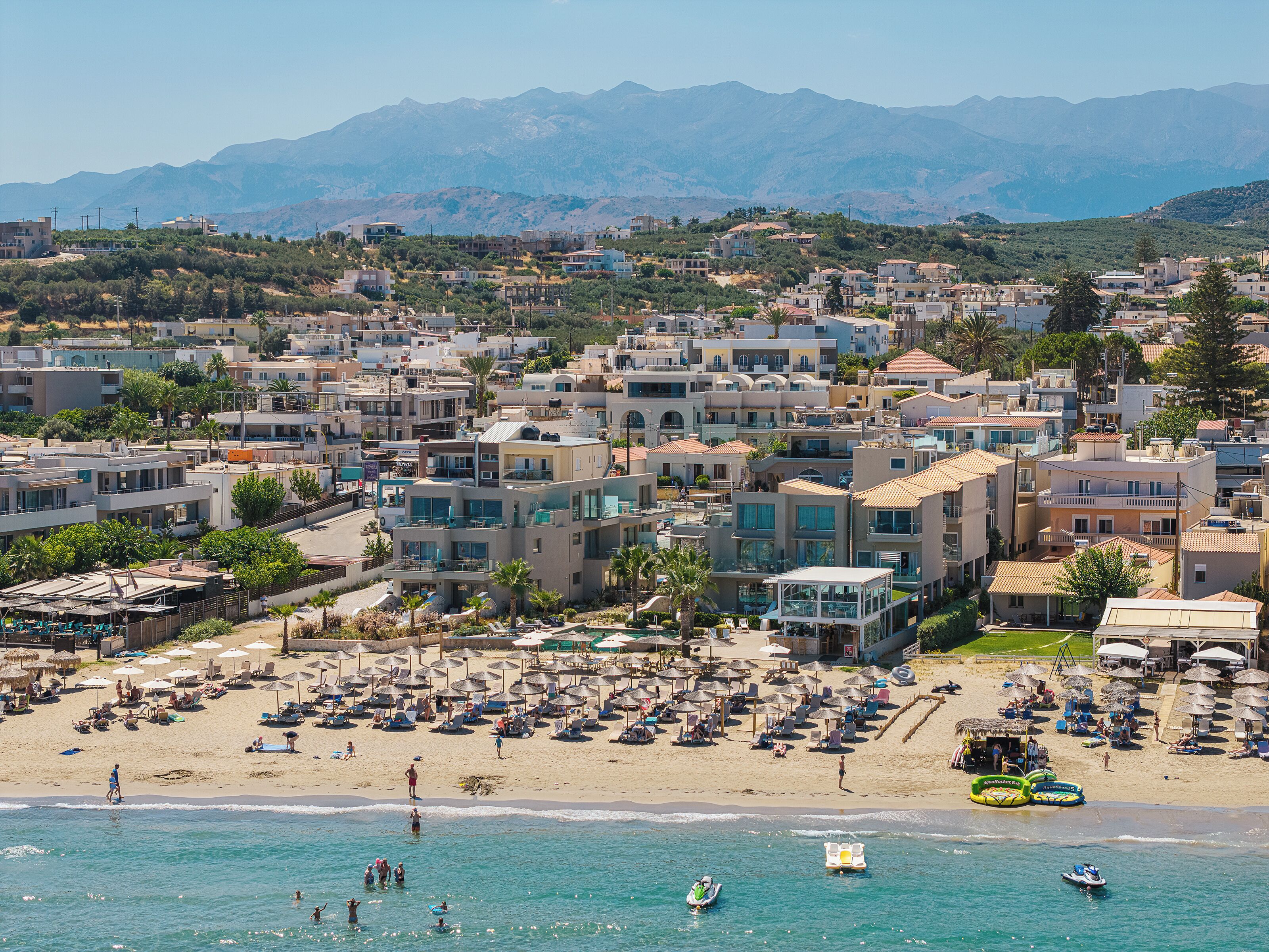 Un pueblo costero con playa, edificios y montañas al fondo.